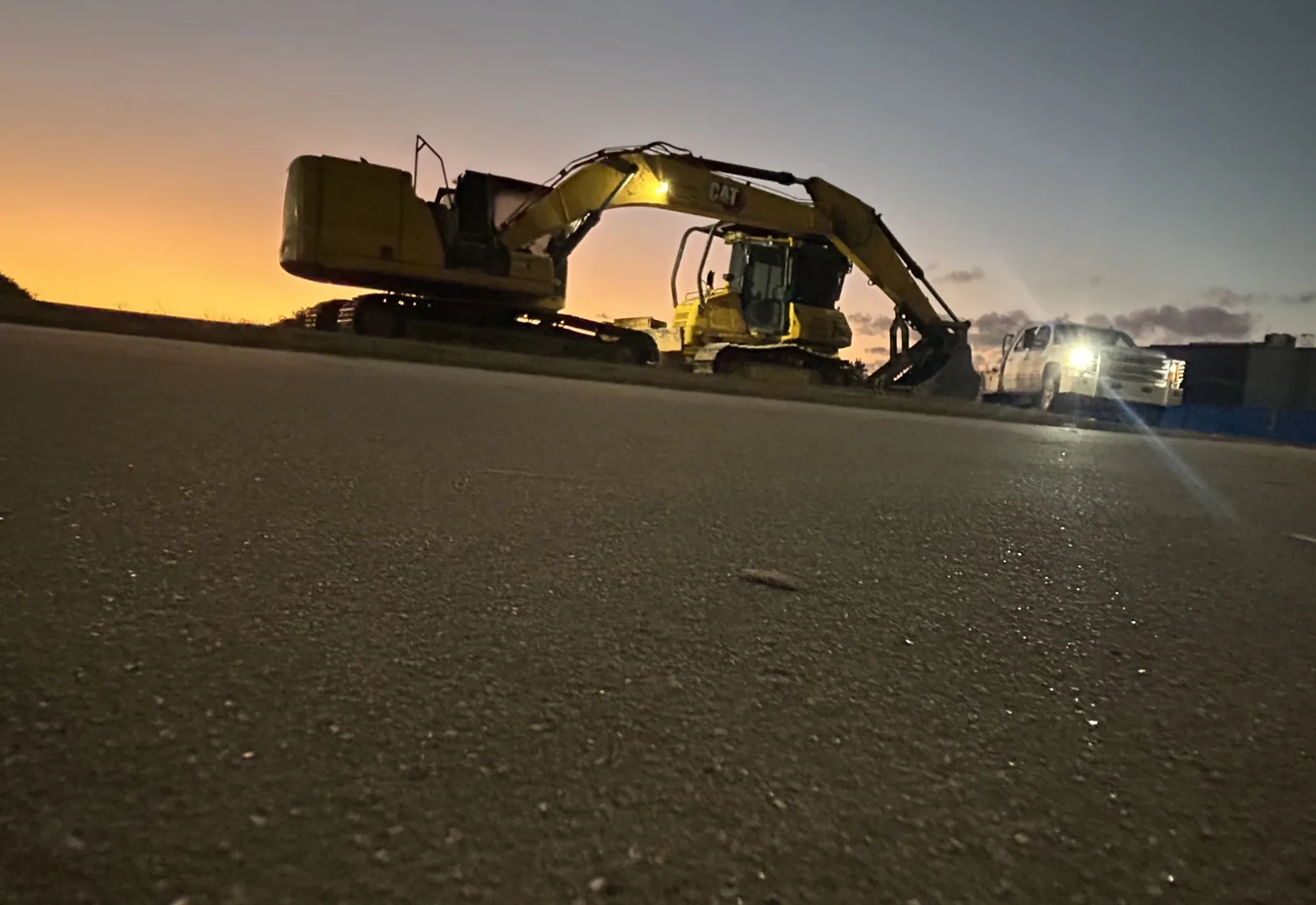 Excavator and the crew truck on a concrete pad at dusk