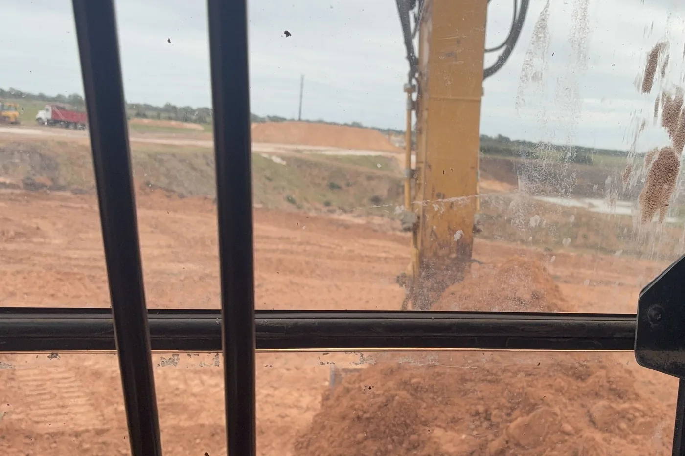 View from the excavator cab across a pit floor, a stockpile and a dump truck at the far side
